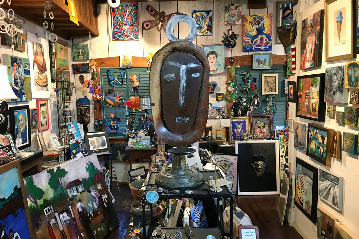 A large brown mask art piece, surrounded by tons of art pieces hanging and leaning everywhere