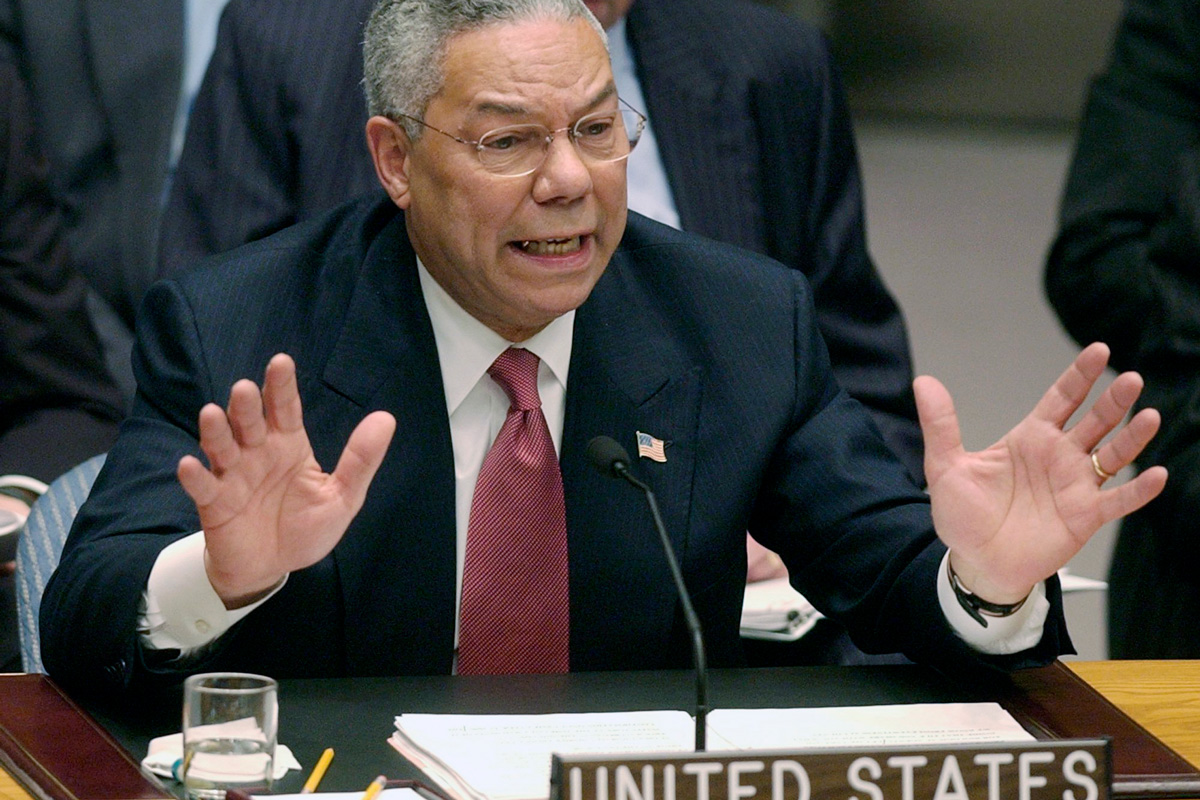Colin Powell, seated behind a microphone and 'United States' nameplate speaks to the United Nations Security Council.