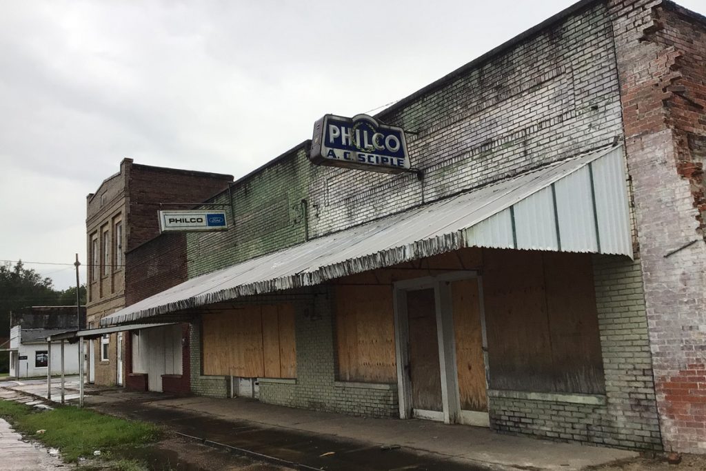 Old brick buildings with dingy whitewash and boarded up windows. A sign for Philco sits above the old white awning