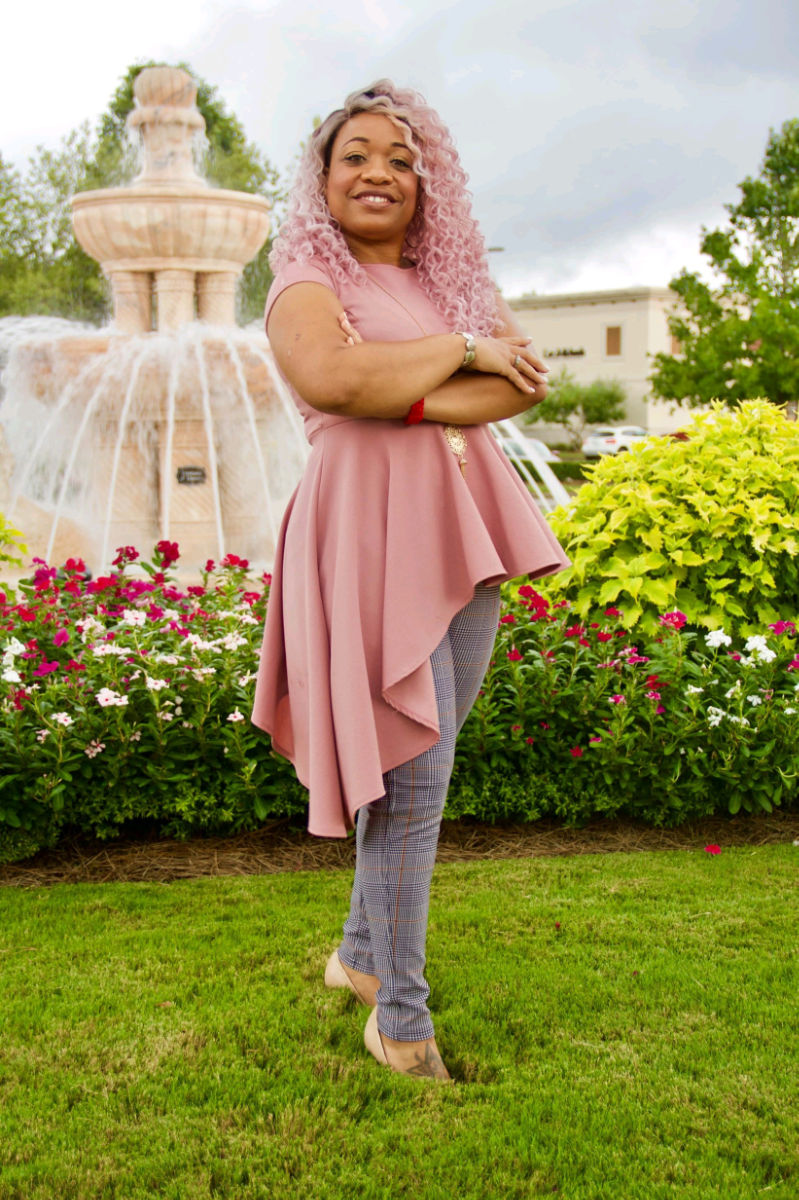 Latysha R. Murry, owner of Da Creator's Image LLC in all pink standing before flowers and a water fountain