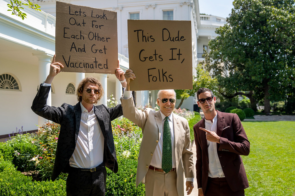 A photo of Biden holding up a sign next to Seth Phillips. Phillips' sign says: "Let's Look Out For Each Other and Get Vaccinated." Biden's sign says "This Dude Gets It, Folks"