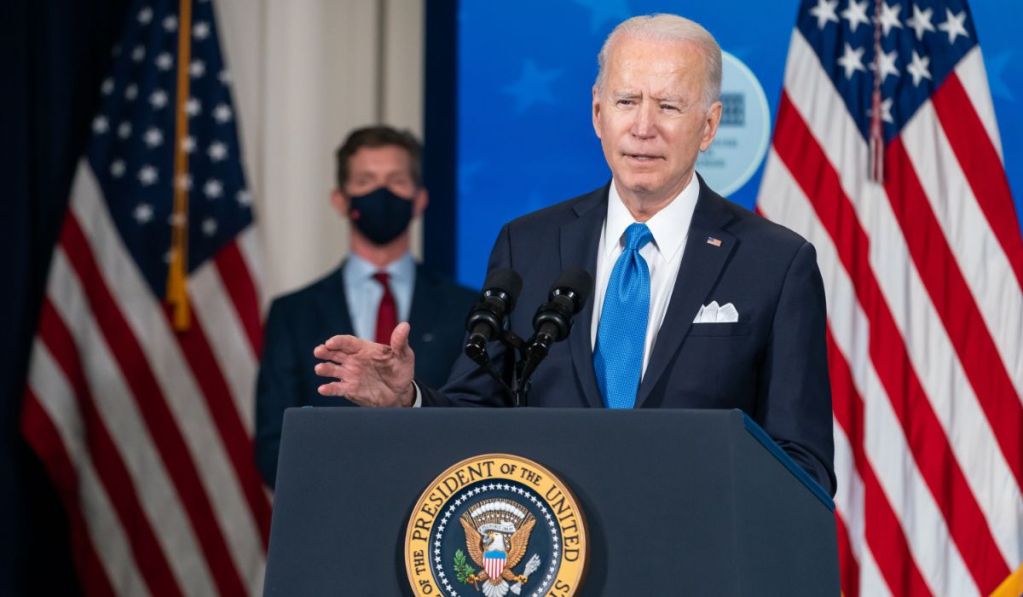 Joe Biden speaking at a podium with two American flags behind him.
