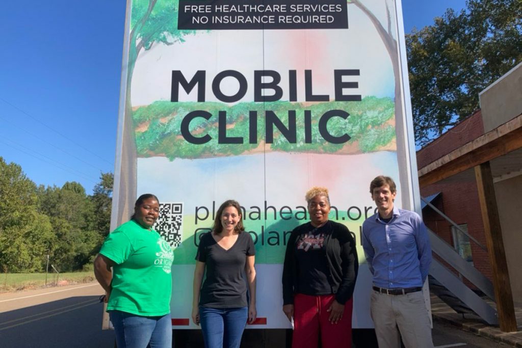 Mobile Clinic truck offering free healthcare services. Four people stand in front of it.