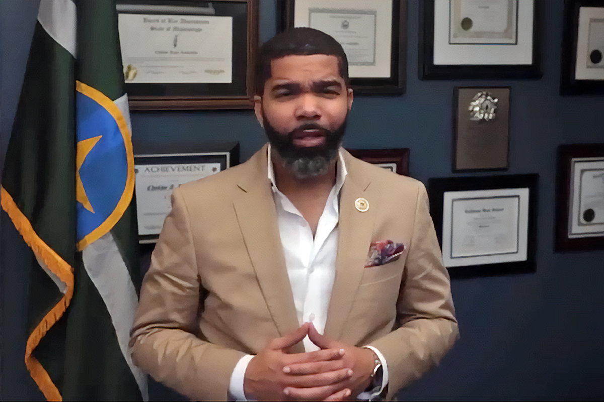 Mayor Chokwe A. Lumumba speaking inside, flanked by the city flag and certificates