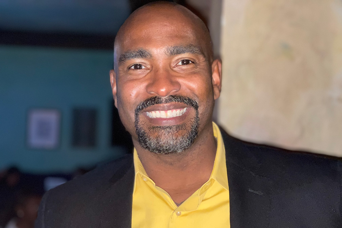 Smiling headshot of Tyree Jones in a yellow shirt and black suit
