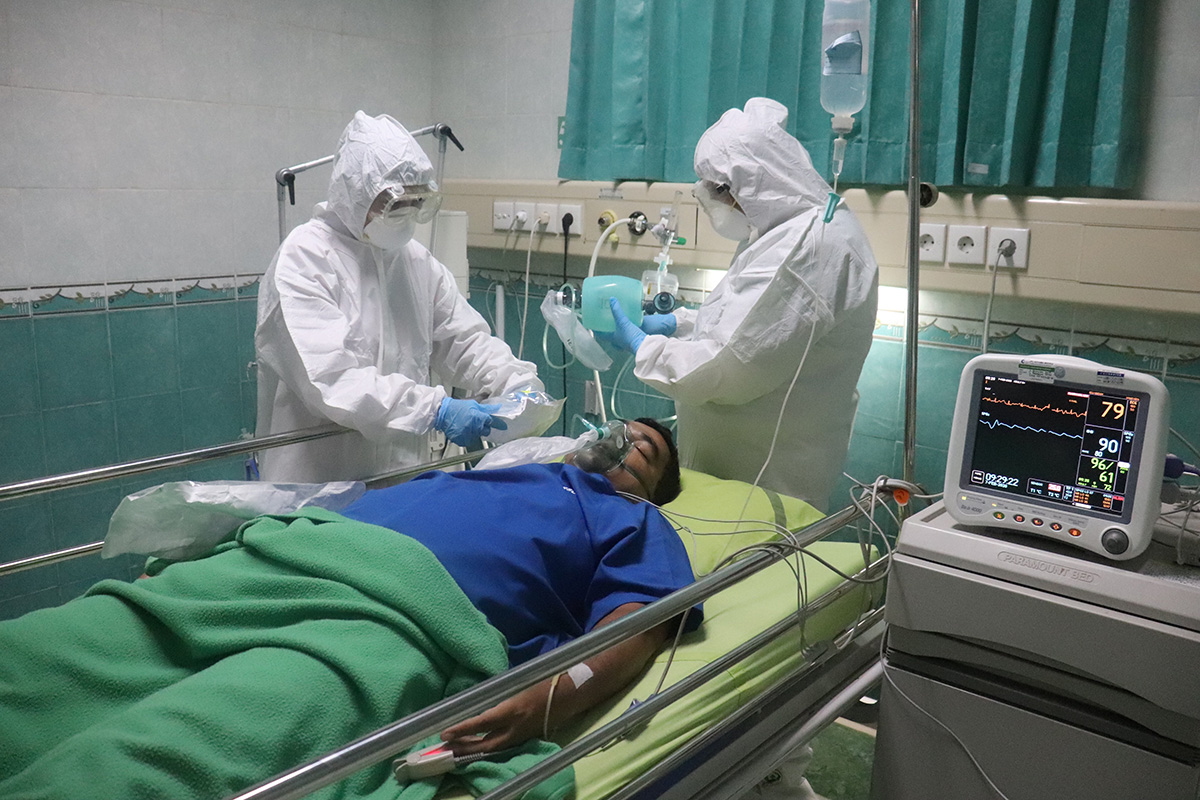 Patient in bed while doctors in white protective gear attend to him