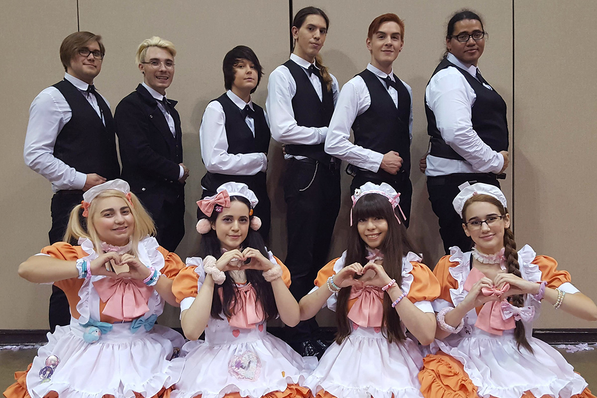 A group of men in black dress clothes with white shirts, and women in orange and white maid costumes
