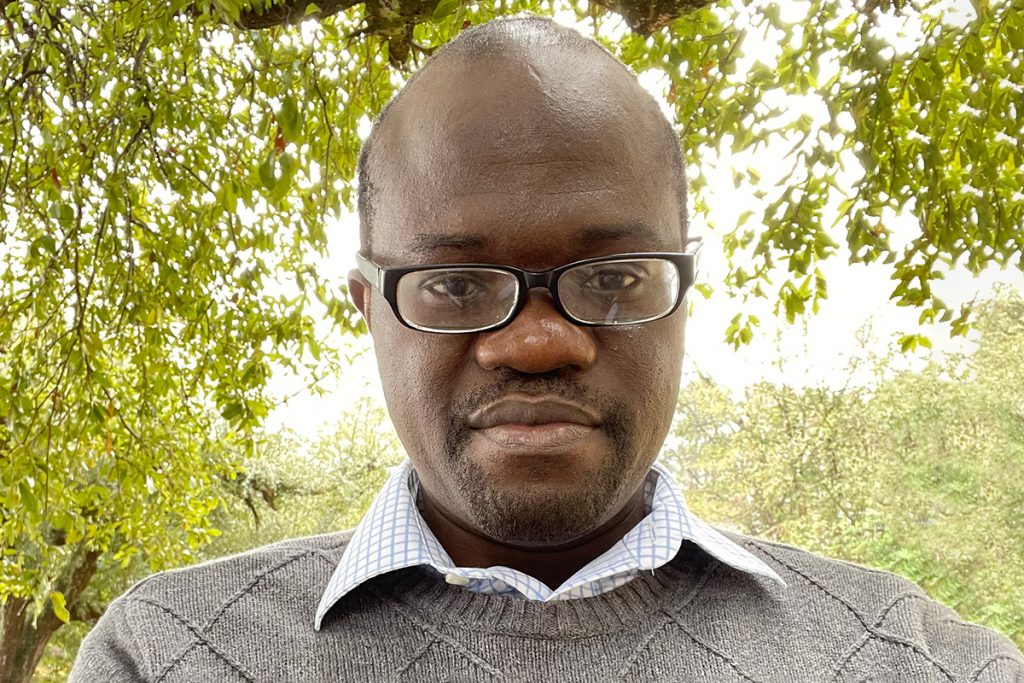 Headshot of Kayode Crown, wearing a grey sweater and black rectangle glasses