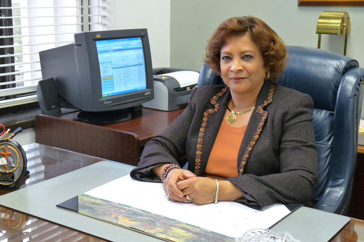Woman in a grey suit jacket and orange top sitting at a desk