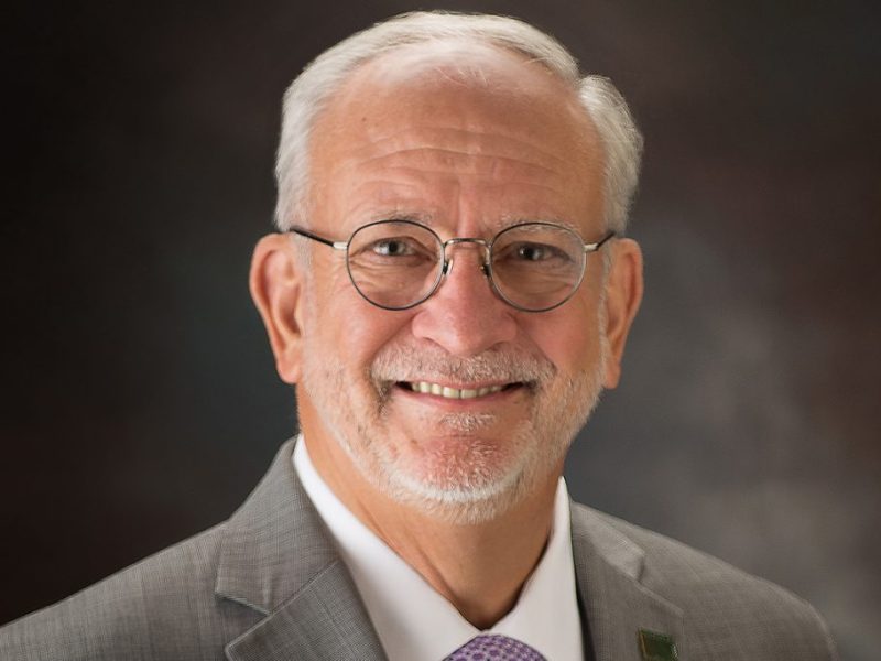 Headshot of a man wearing a light grey suit and glasses