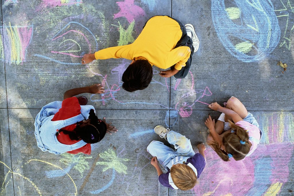 Four children (7-10) drawing with chalk on pavement, overhead view