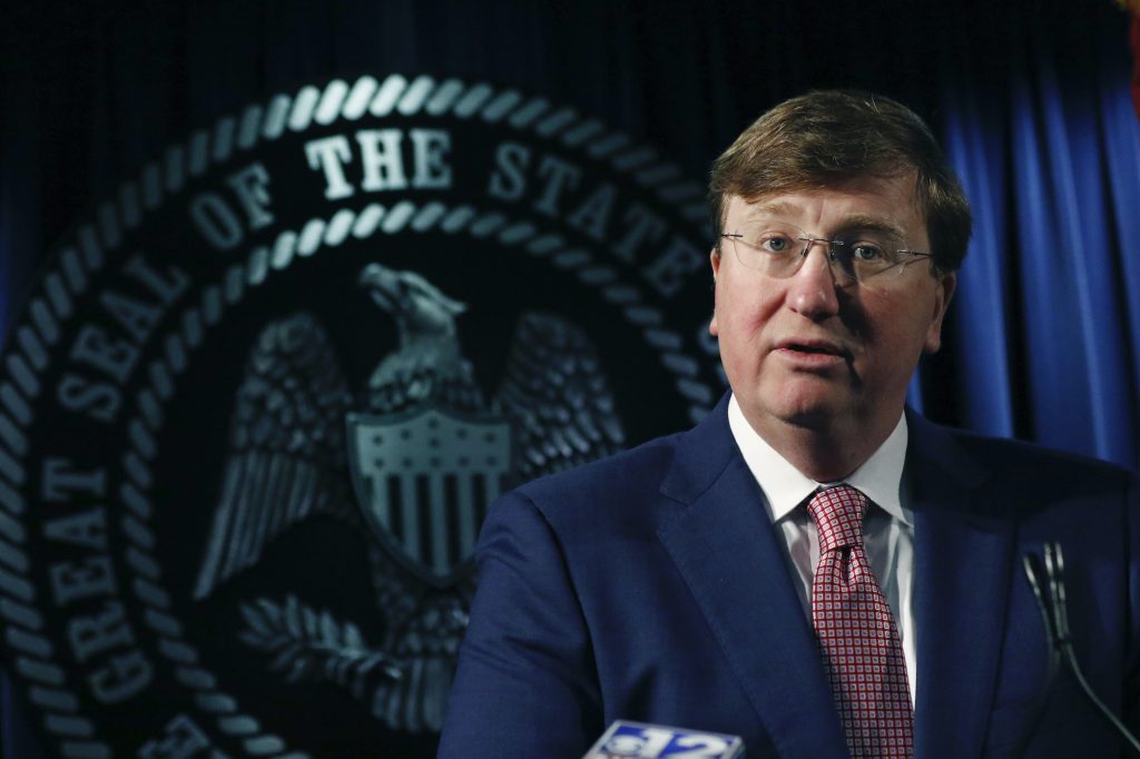 a photo of Tate Reeves speaking in front of the state seal