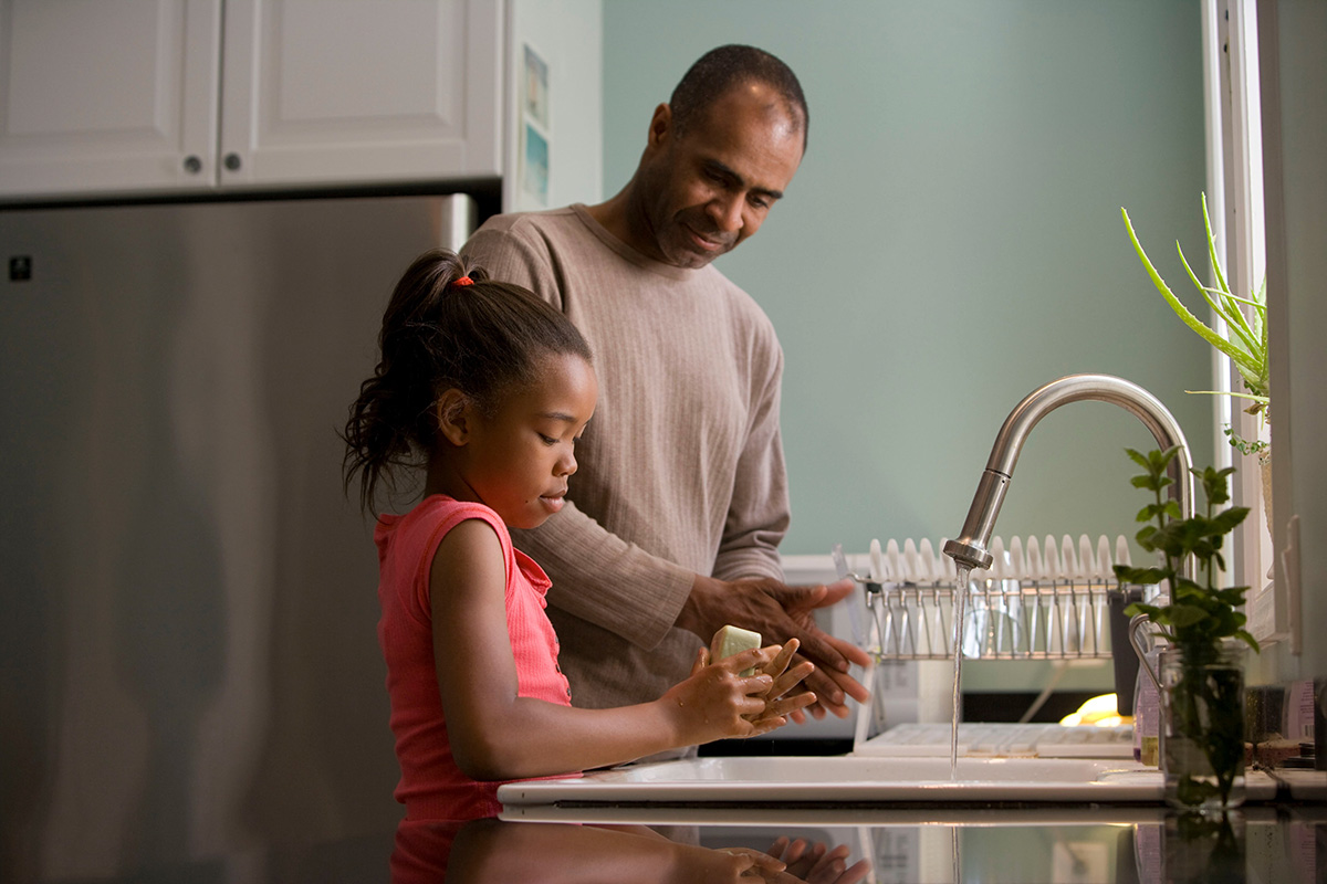 Black father and daughter washing their hands at the sink