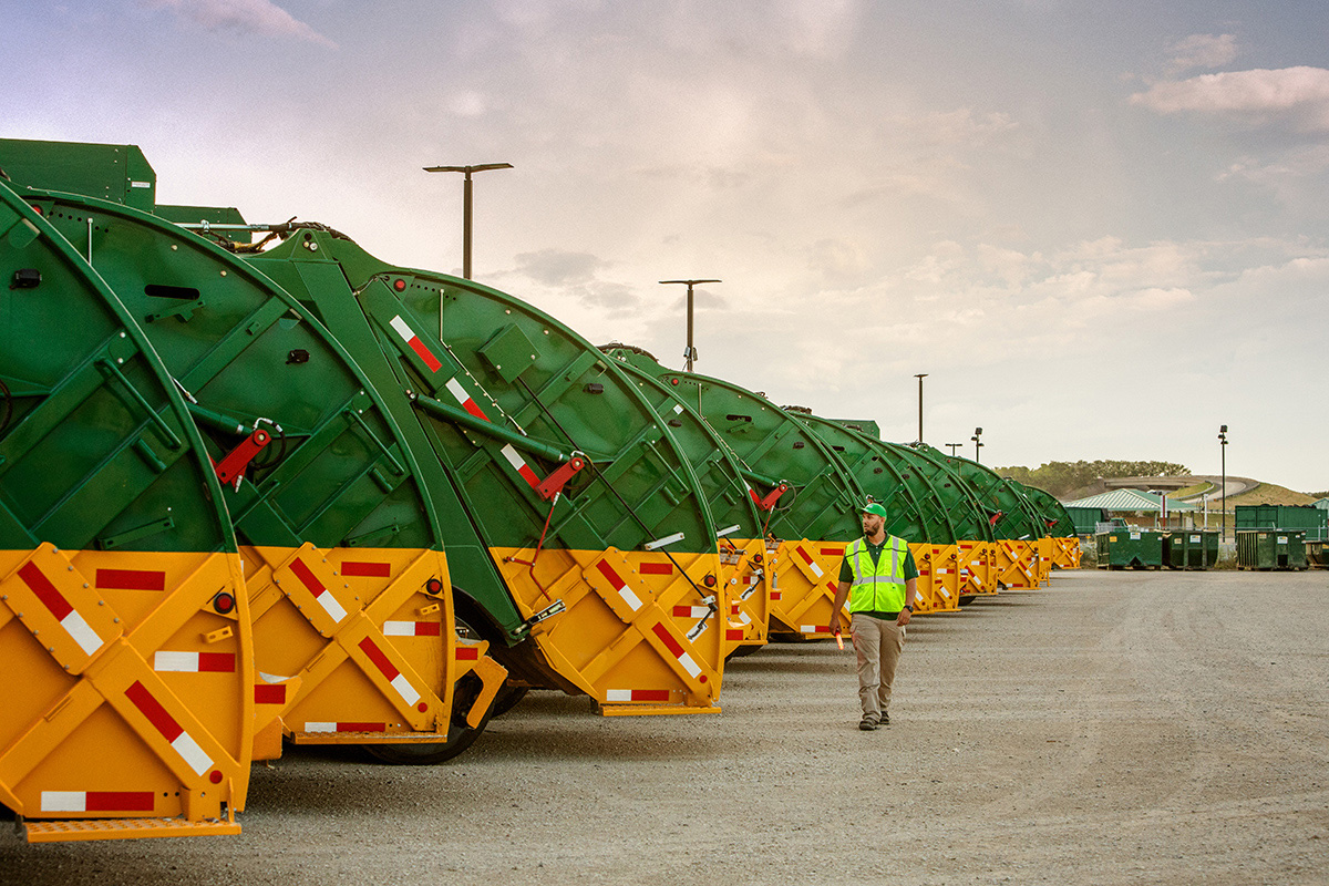 A row of green and yellow trash trucks parked outside