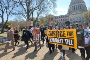 A group of people marching in front of the Mississippi state capitol building with signs and pictures of Emmett Till