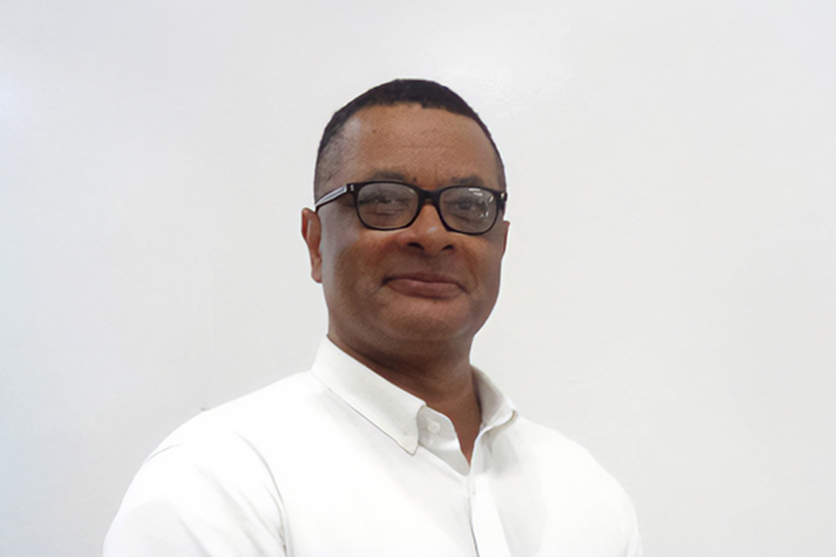 Dr. Roscoe Barnes III in a white shirt and black glasses against a white wall