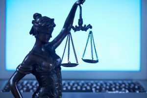 A statue of blind justice holding her scales backlit by a blue monitor