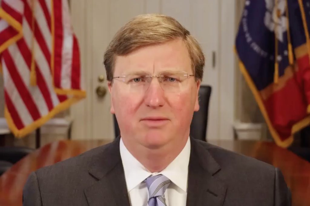 a photo of Governor Tate Reeves looking straight into the camera with an American and Mississippi flag behind him