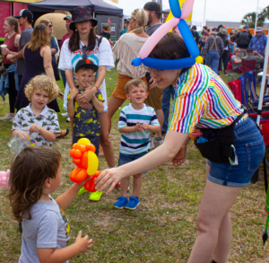Colorful lady handing balloon animal to children