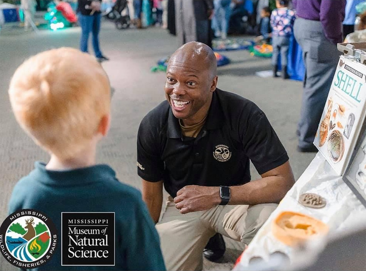 A man in work outfit leaning in front of an educational table to talk to a child