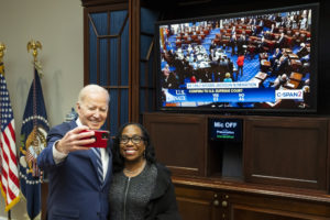 a photo of Joe Biden holding up a phone to take a selfie with Judge Ketanji Brown Jackson in front of a TV showing her 53-47 confirmation vote