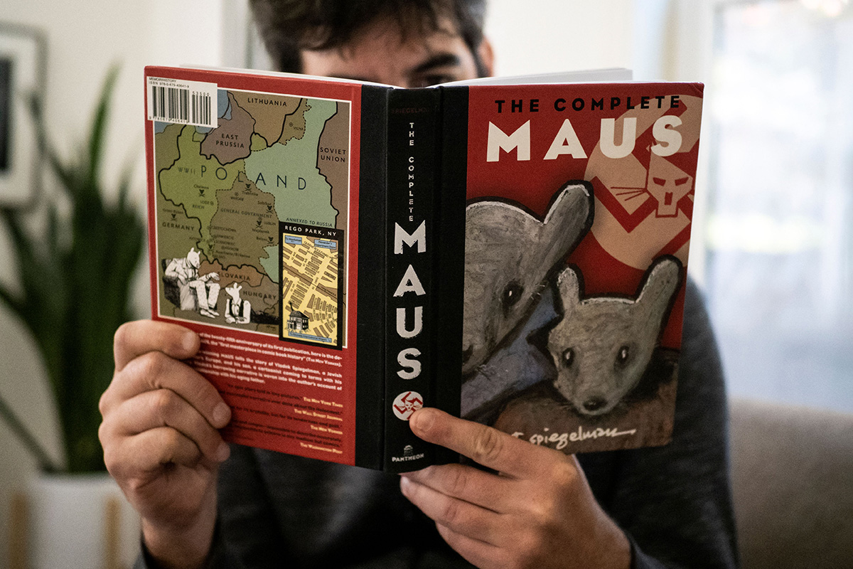 A teenage boy reads a book with the title 'Maus.