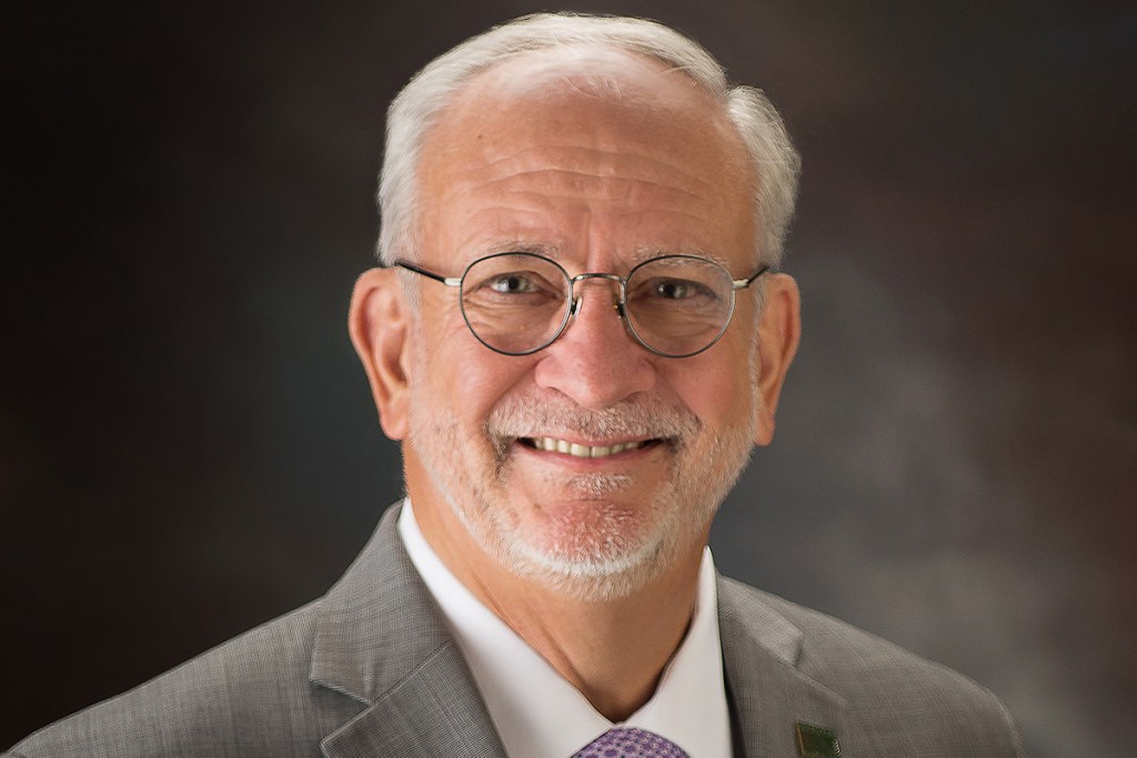 Headshot of a man wearing a light grey suit and glasses