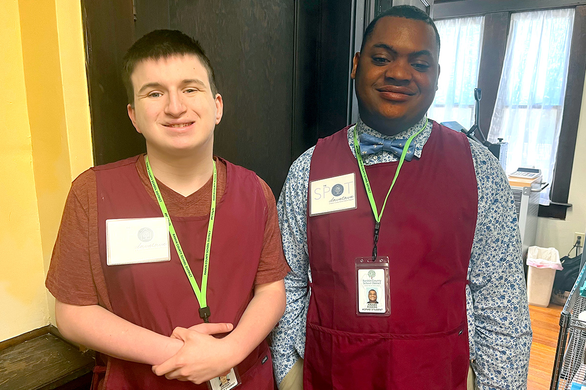 Two men in red vests smile to the camera