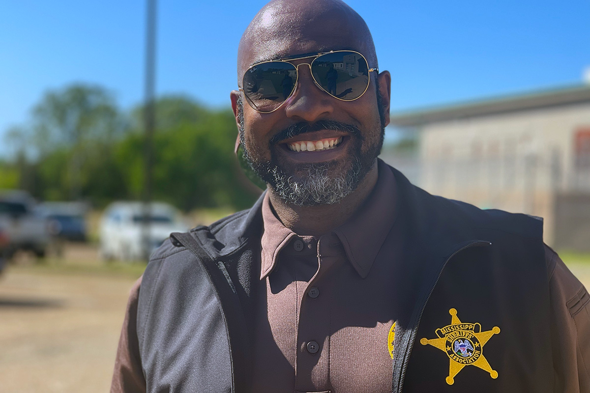A smiling bearded man in sunglasses, wearing a sheriff uniform