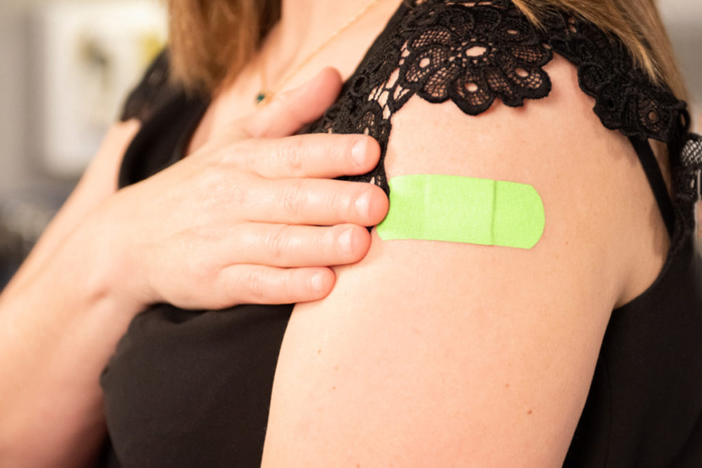 Close up of a woman's arm with a bright green bandaid on her upper arm