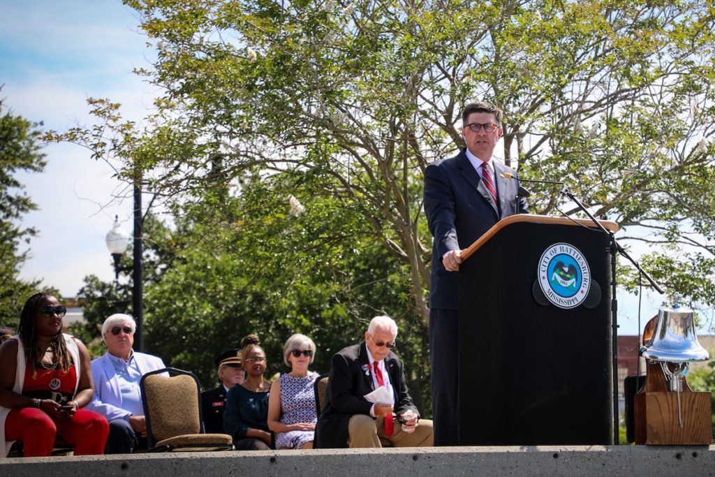 a photo of a man standing at a podium in front of a crowd of people outdoors