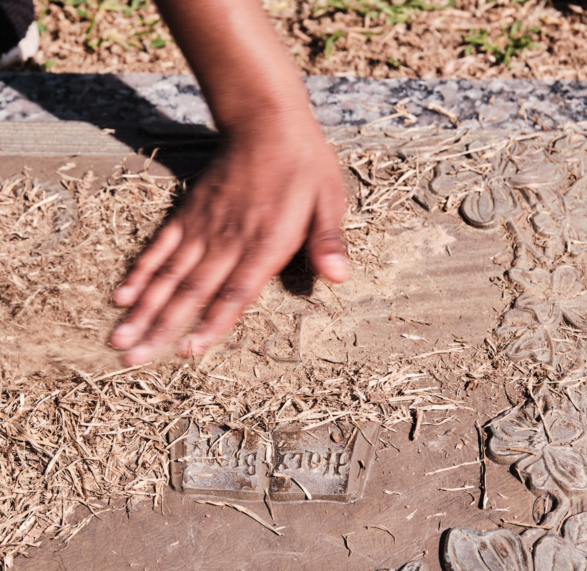 A hand is wiping grass and soil away from a grave marker with Holy Bible embossed