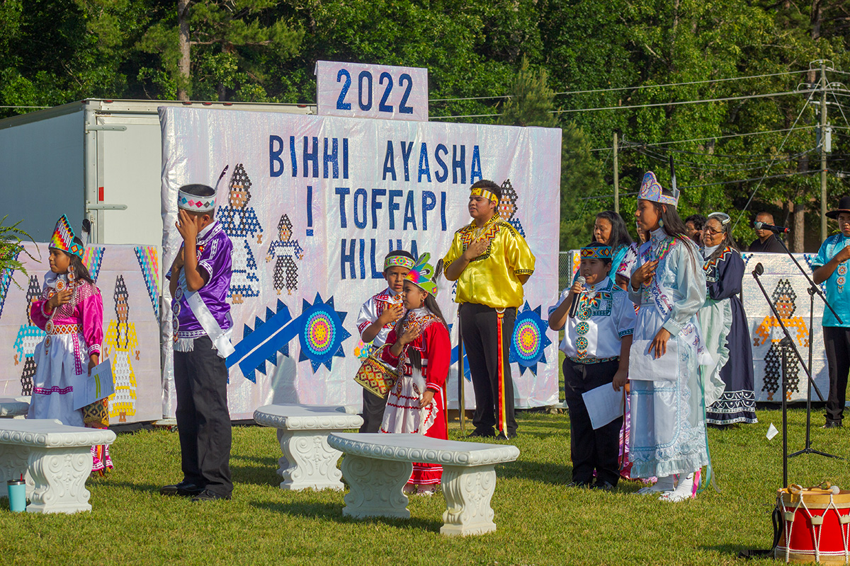 Young people in colorful dress standing in front of a sign that says 2022 Bihhi Ayasha Toffapi Hilha