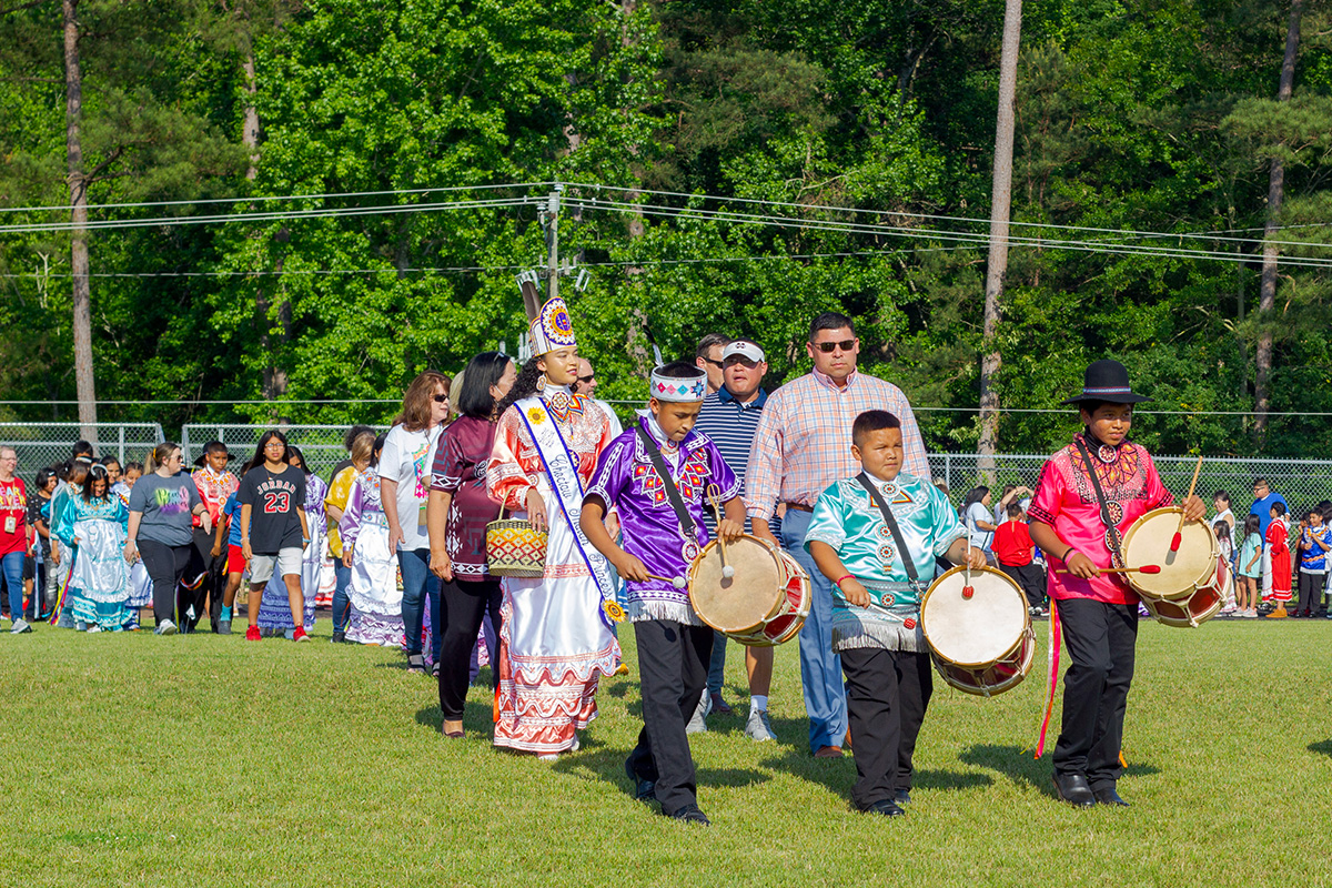 Boys with drums lead a long line of people in colorful dress