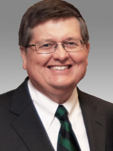 Headshot of Dan Edney in a dark suit and dark green striped tie
