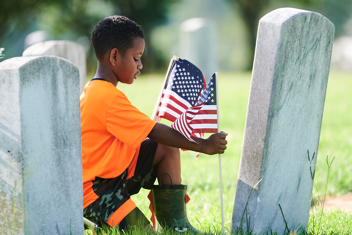A child in orange and camo kneels to place US Flags in front of veteran graves