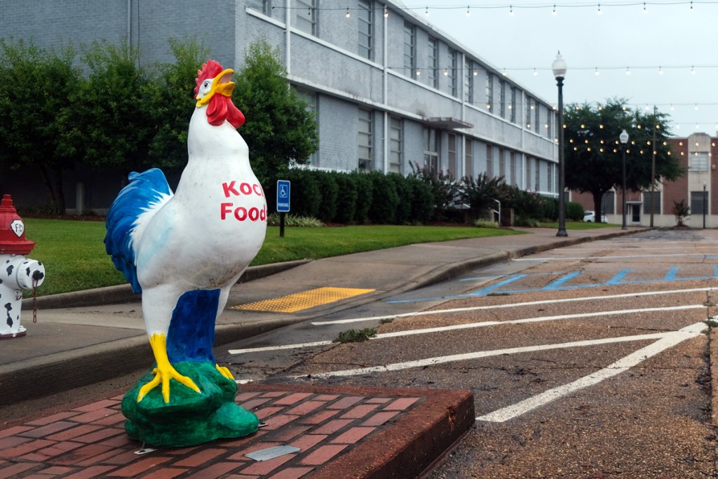 A chicken with Koch Foods written on the chest stands in front of a building