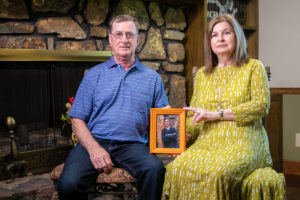 Two people sit beside a fireplace holding a framed photo