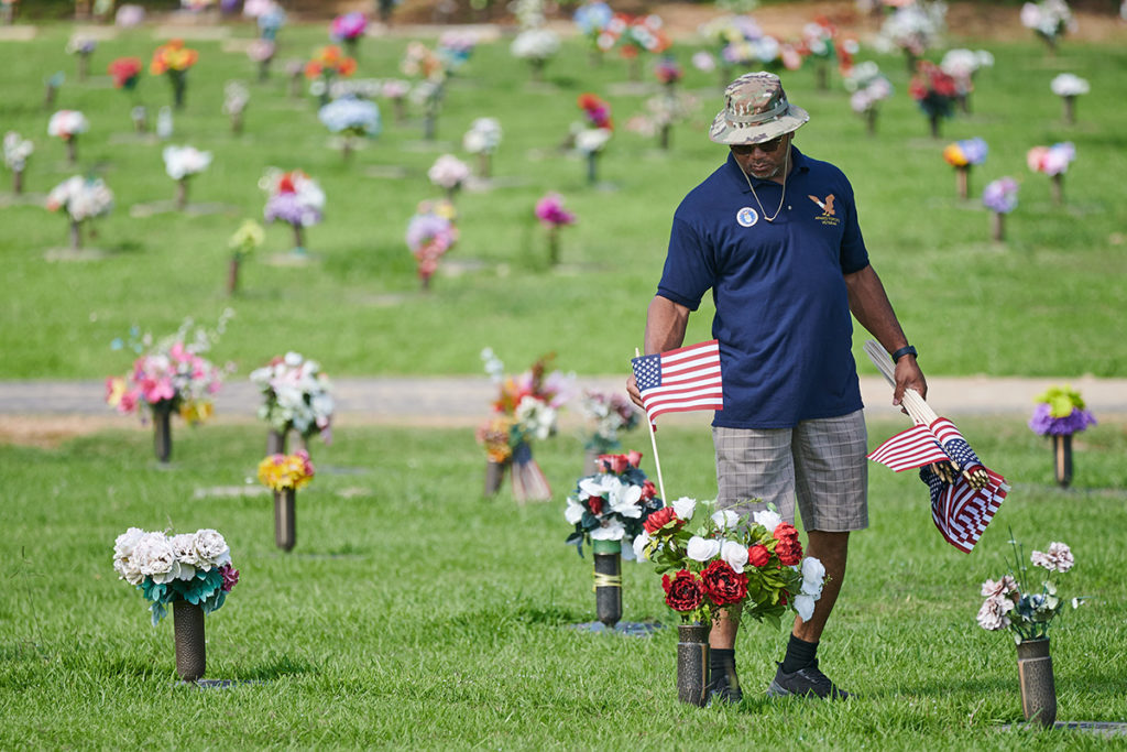 A man in blue places US Flags at gravesites