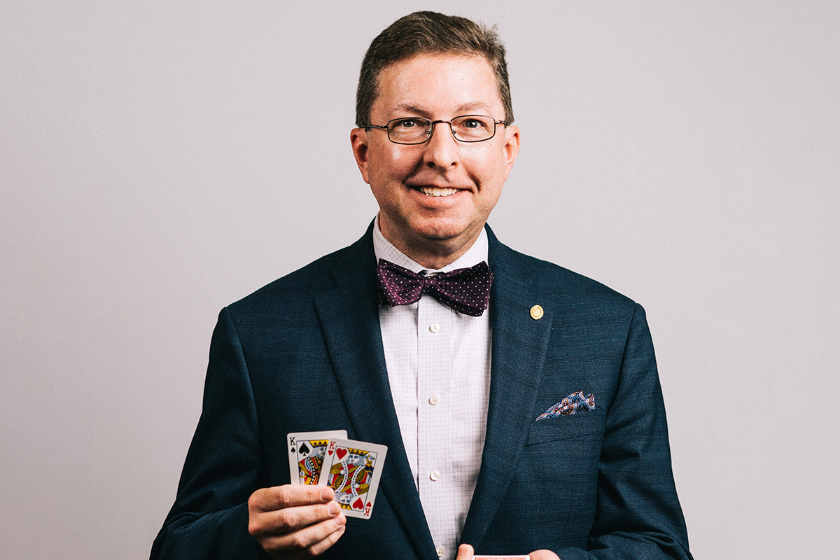 A magician in a black suit holding up cards