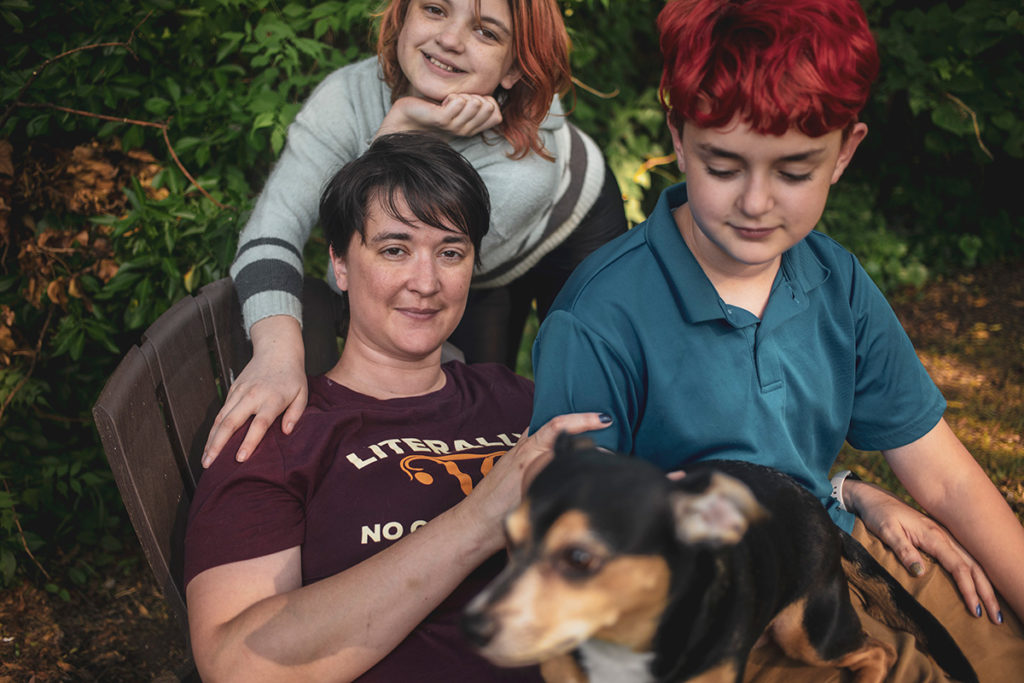 A woman sits outside with two kids and a dog in her lap