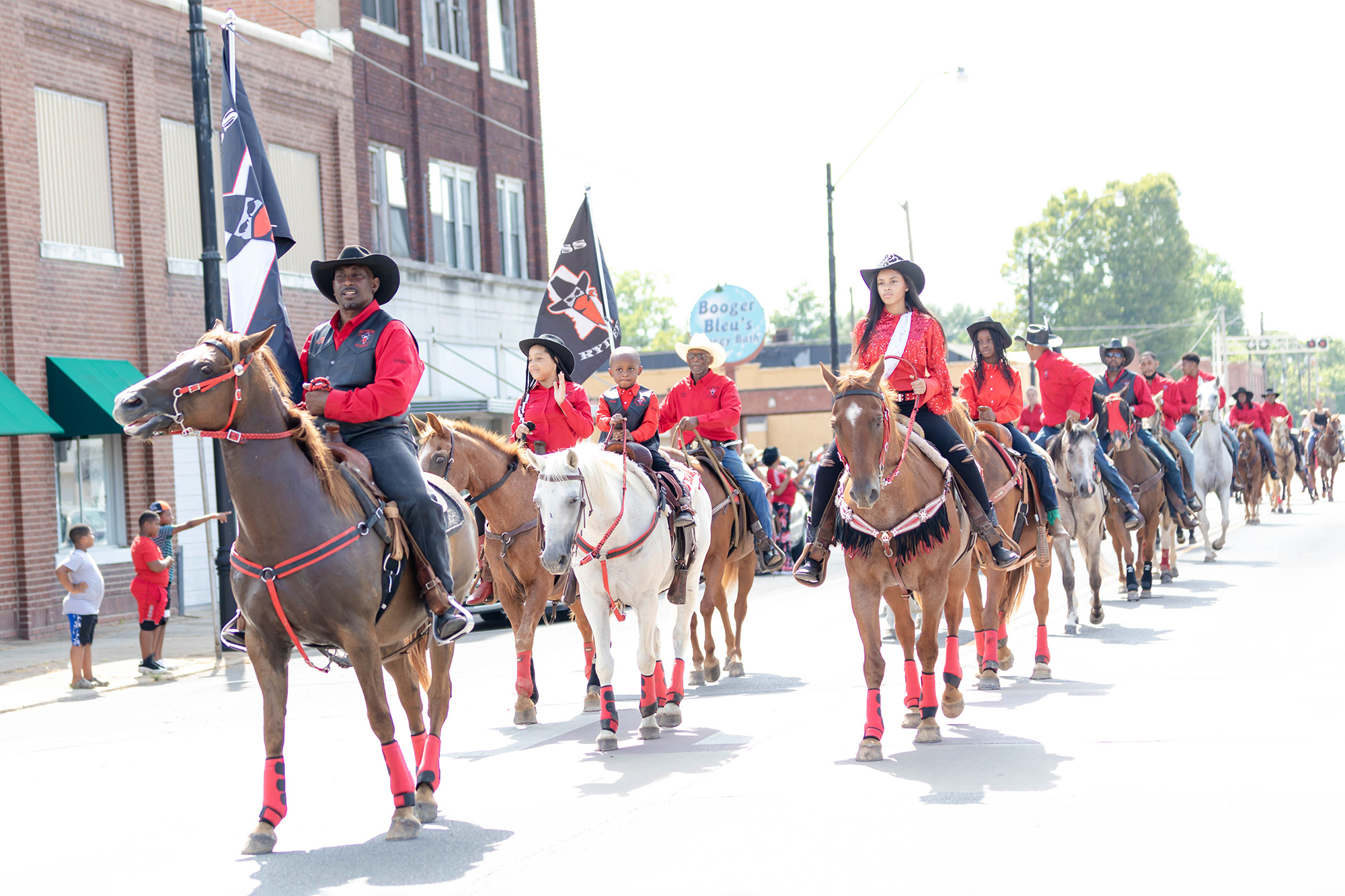 A group of black cowboys wearing black and red, riding horses