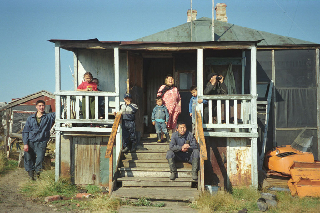A family of people in Siberia stand on and around their front porch