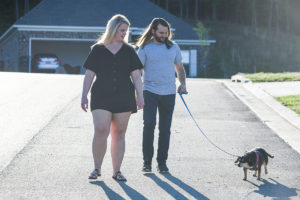 A man and a woman walk a dog on a leash down a neighborhood roadway