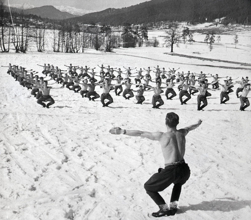 Rows of shirtless men exercising in the snow.