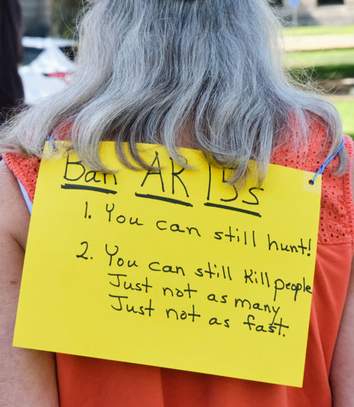 A yellow sign hanging on the back of a woman reading BAN AR 15s