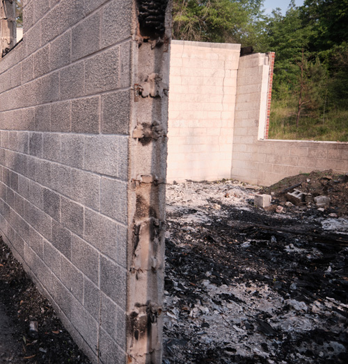 A grey concrete wall gives way to burnt debris of the building