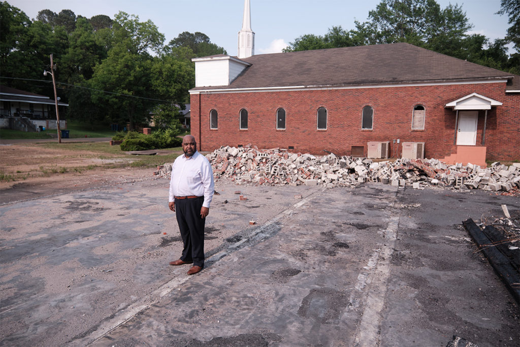 A man stands on the concrete slab of an old building, brick rubble in the background