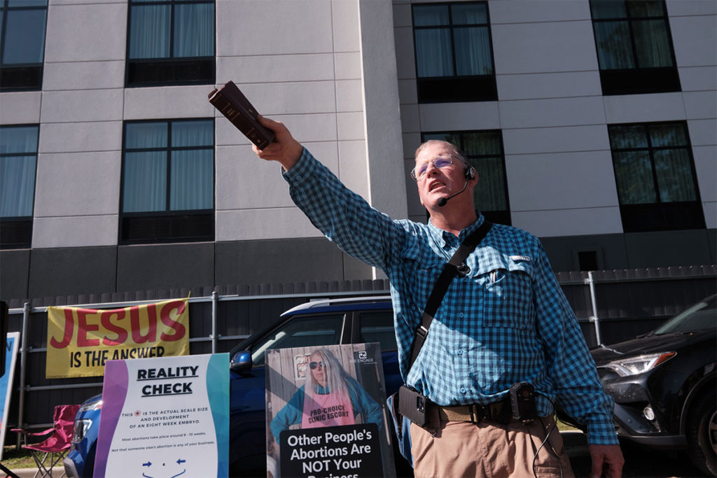An abortion protestor speaks with arm raised in front of protestor signs