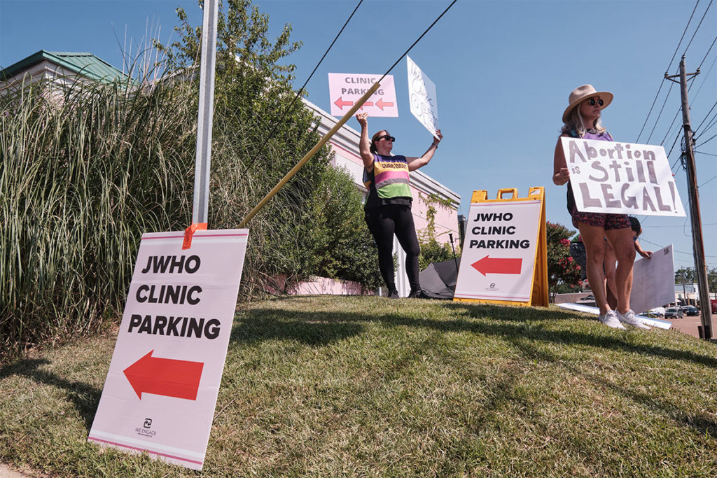 Women stand on a grassy hill holding signs that stay "Abortion is still legal"